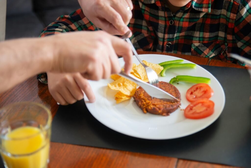 pexels-photo-7492948-7492948 A parent helps a child slice breakfast food, guiding their eating habits.